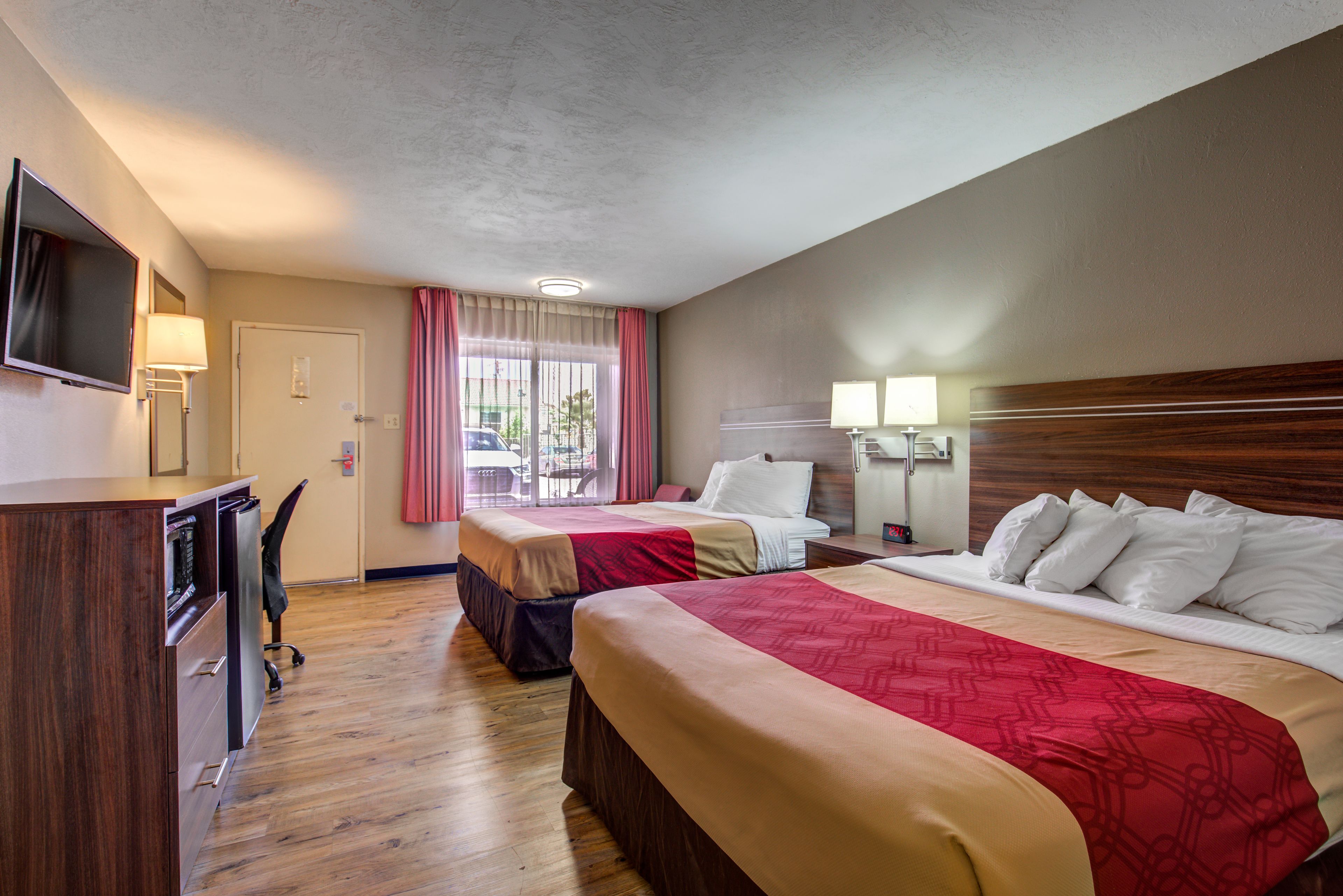 A hotel room with two beds, a desk, a TV, and a window with curtains.