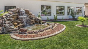 A modern building with a landscaped garden featuring a rock waterfall and a circular stone border.