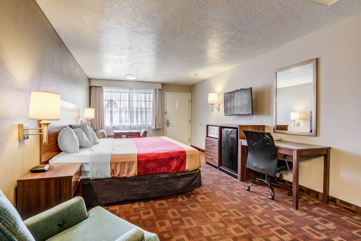 Une chambre d’hôtel avec un lit, un bureau, une chaise, une télévision et une fenêtre avec des rideaux.