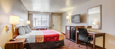 Habitación de hotel con cama, escritorio, silla, televisor y ventana con cortinas.