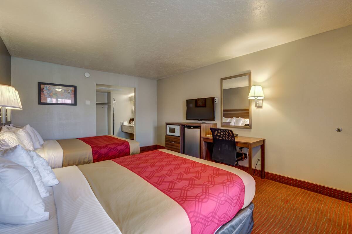 Une chambre d’hôtel avec deux lits, un bureau avec un ordinateur, une télévision et un miroir.