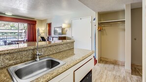 A kitchen with a granite countertop, stainless steel sink, and a built-in dishwasher. There is a window with red curtains and a view of the outdoors.