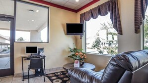 A lobby with a leather sofa, a small table with a vase of flowers, a desk with a computer, and a large mirror.