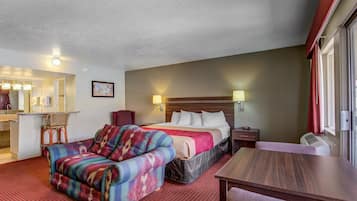 A hotel room with a bed, a sofa, a desk, a chair, a mirror, and a window.
