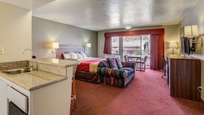 A hotel room with a kitchenette, a bed, a sofa, a dining table, and a view of the outside.