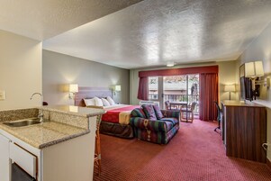 Habitación de hotel con kitchenette, una cama, un sofá, una mesa de comedor y vistas al exterior.