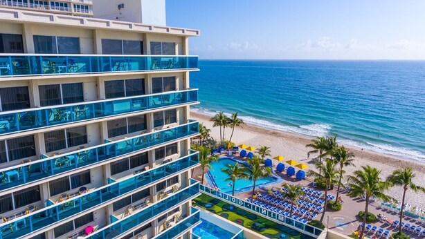 A hotel with multiple balconies overlooking a beach and a pool area with sun loungers and umbrellas.