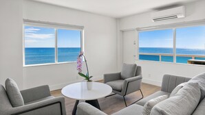 A modern living room with a view of the sea, a round white table, and grey furniture.