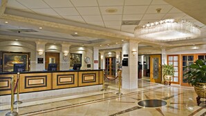 A hotel lobby with a reception desk, a large chandelier, marble flooring, and a statue.
