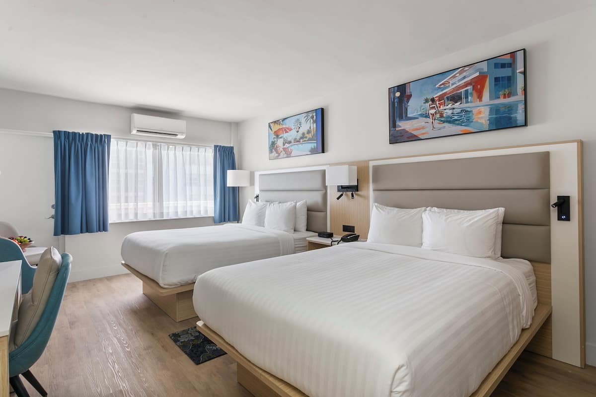 A hotel room with two beds, a desk, a chair, and artwork on the walls.