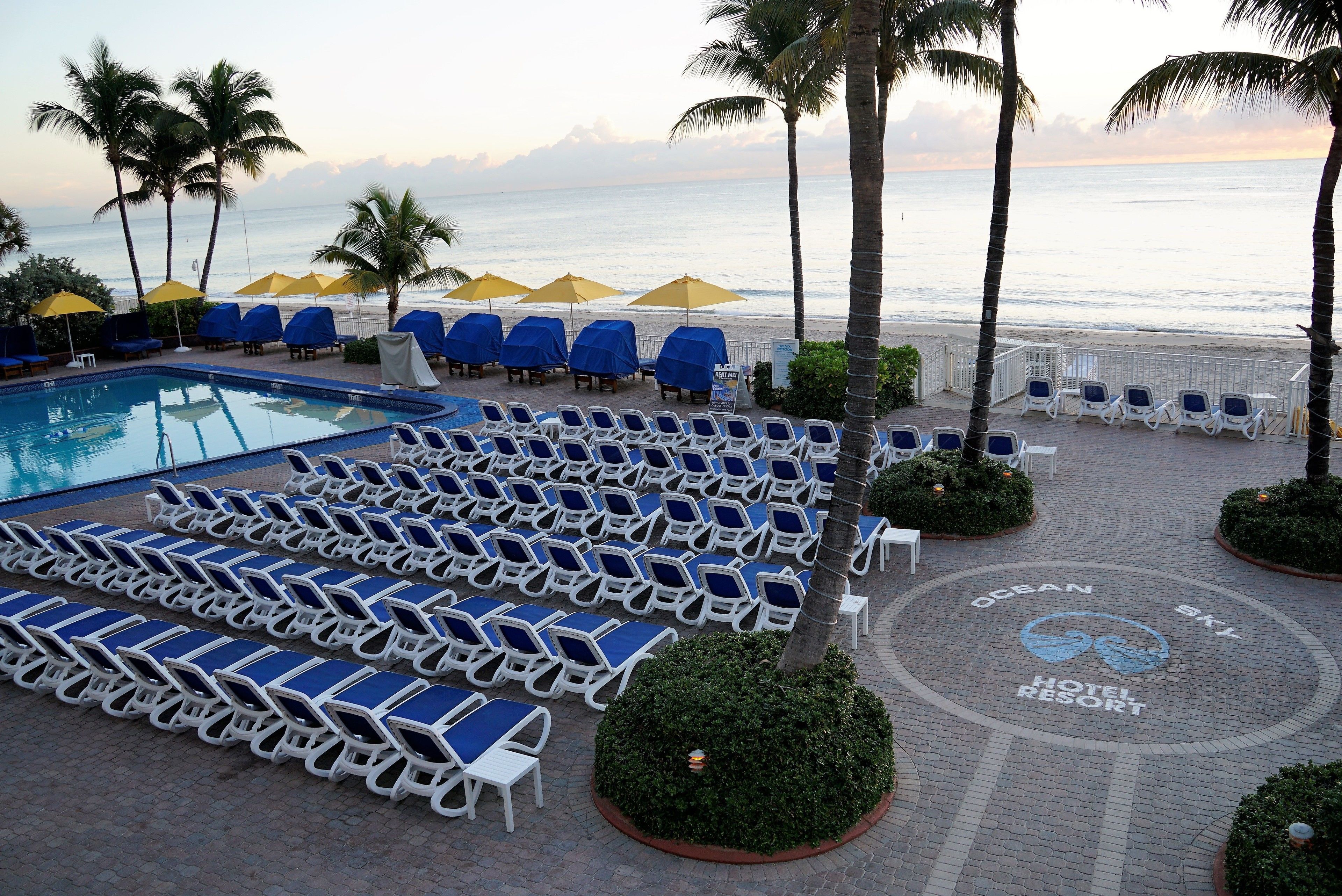 A poolside area with lounge chairs and umbrellas, a pool, and a view of the ocean.