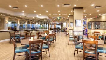 A spacious restaurant with wooden tables and chairs, a high ceiling with recessed lighting, and a view of the dining area through glass partitions.