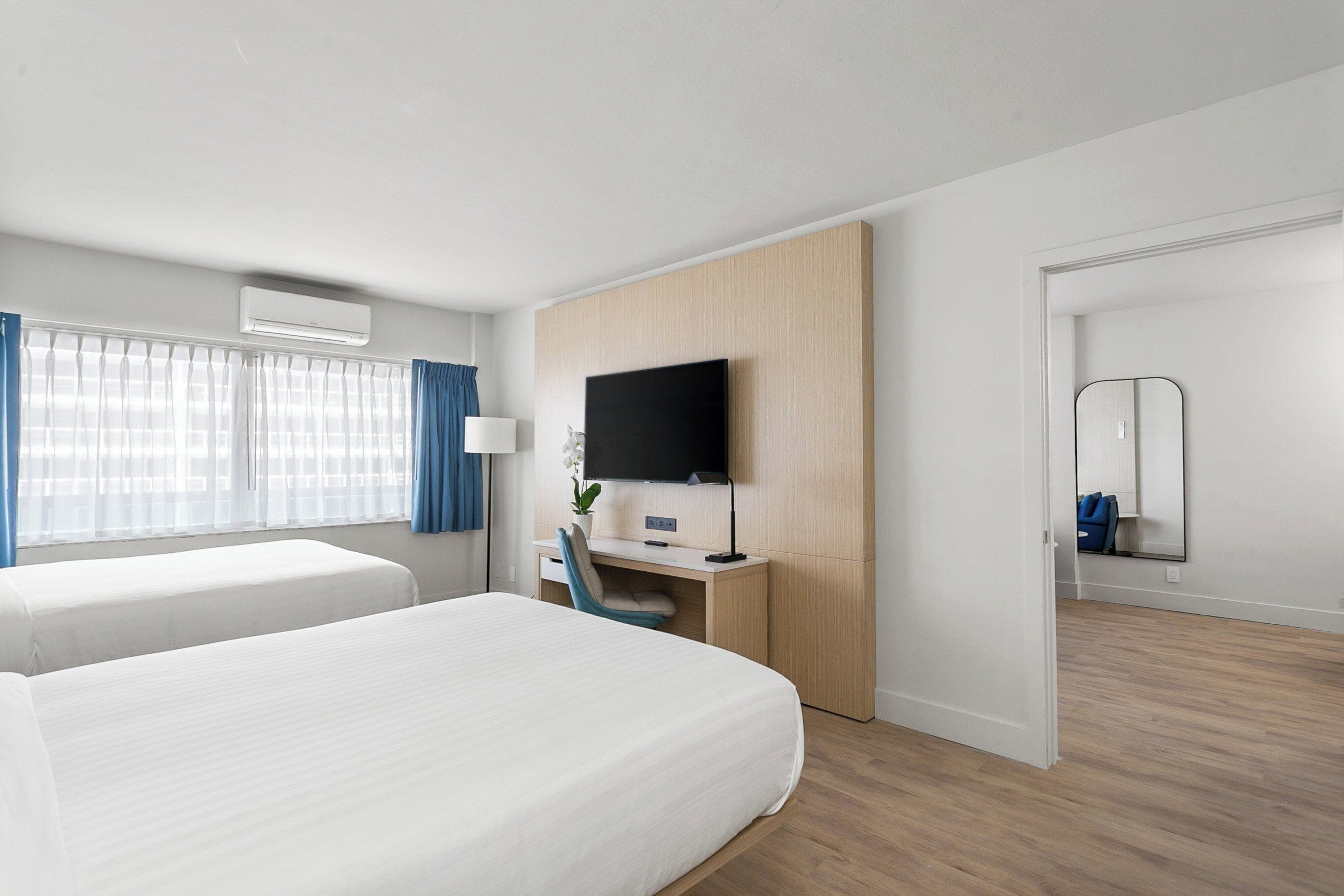Een hotelkamer met twee bedden, een bureau met een computer, een flatscreen televisie en een spiegel aan de muur.