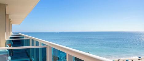A balcony with a glass railing overlooking a beach.