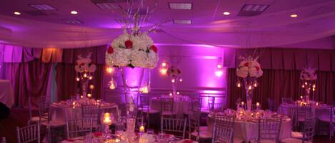 Un salón de banquetes con mesas redondas dispuestas para comidas, cada una con mantel blanco, cubertería y cristalería.