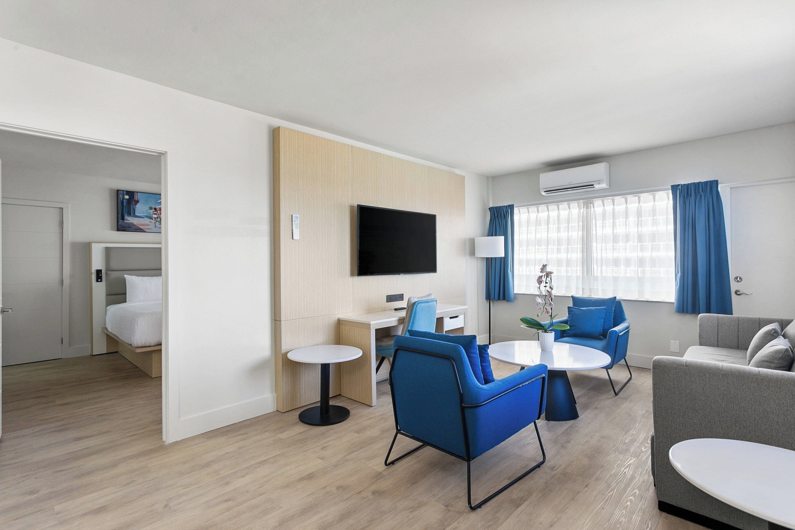 A modern hotel room with a bed, a desk, a TV, a sofa, and a dining table.