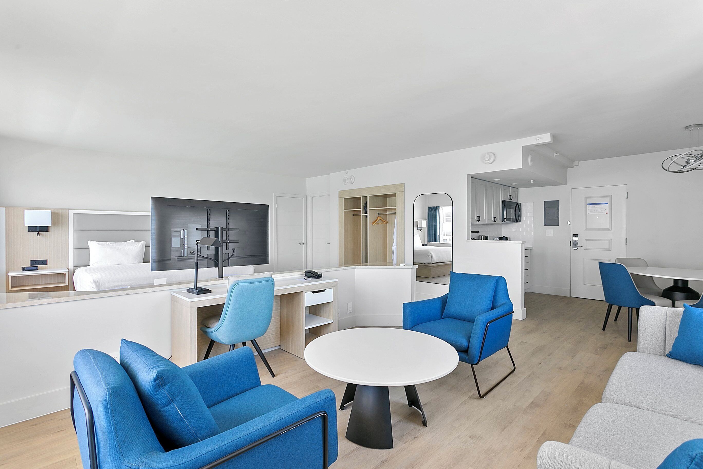 A modern, well-lit living room with a large flat-screen TV, a round dining table, and blue and grey sofas.