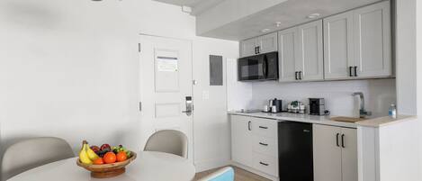 Una cocina moderna con armarios blancos, un microondas negro y una cafetera.