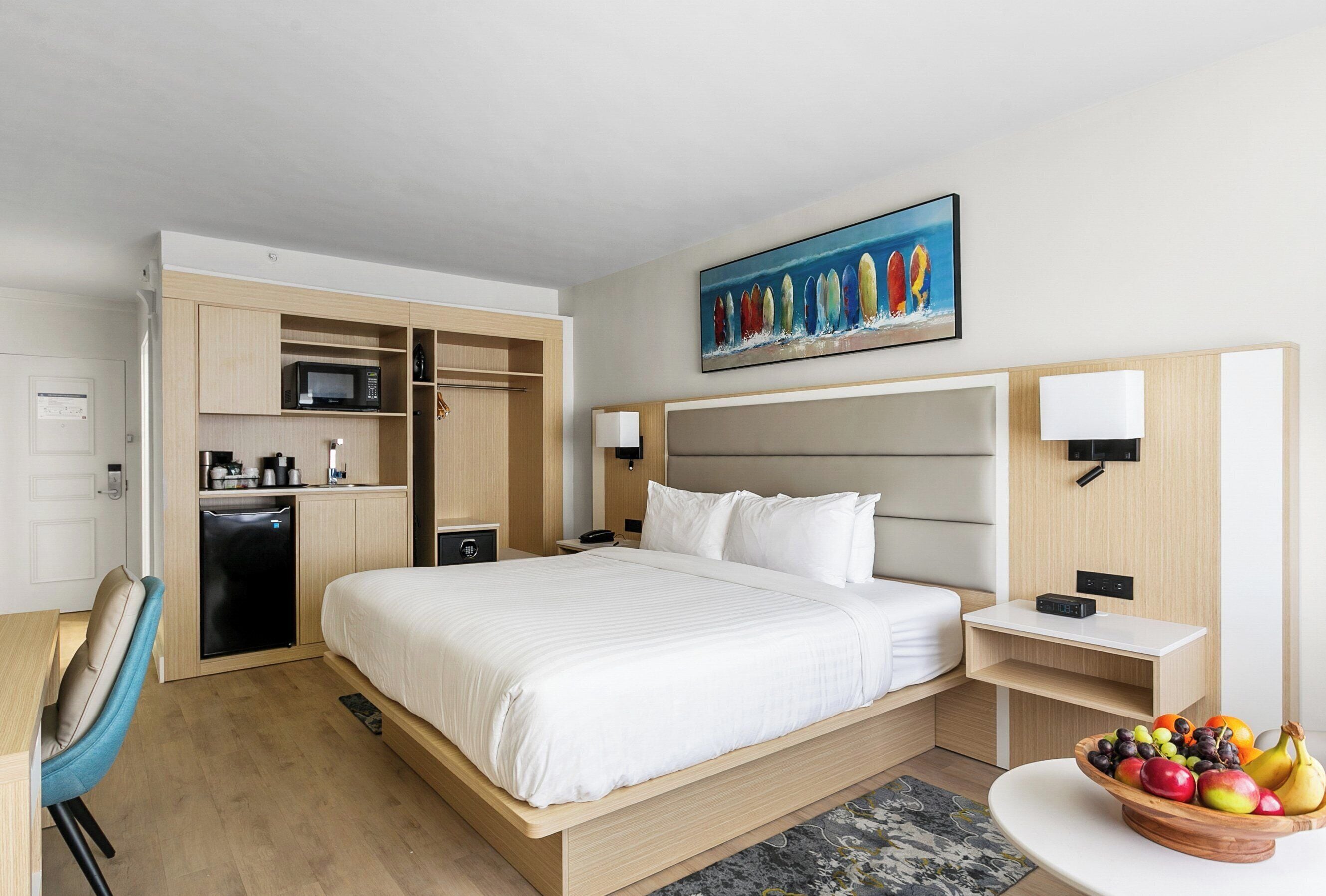 Ein Hotelzimmer mit Bett, Nachttischen, Schreibtisch, Stuhl, Mikrowelle, Kühlschrank und Obstschale.