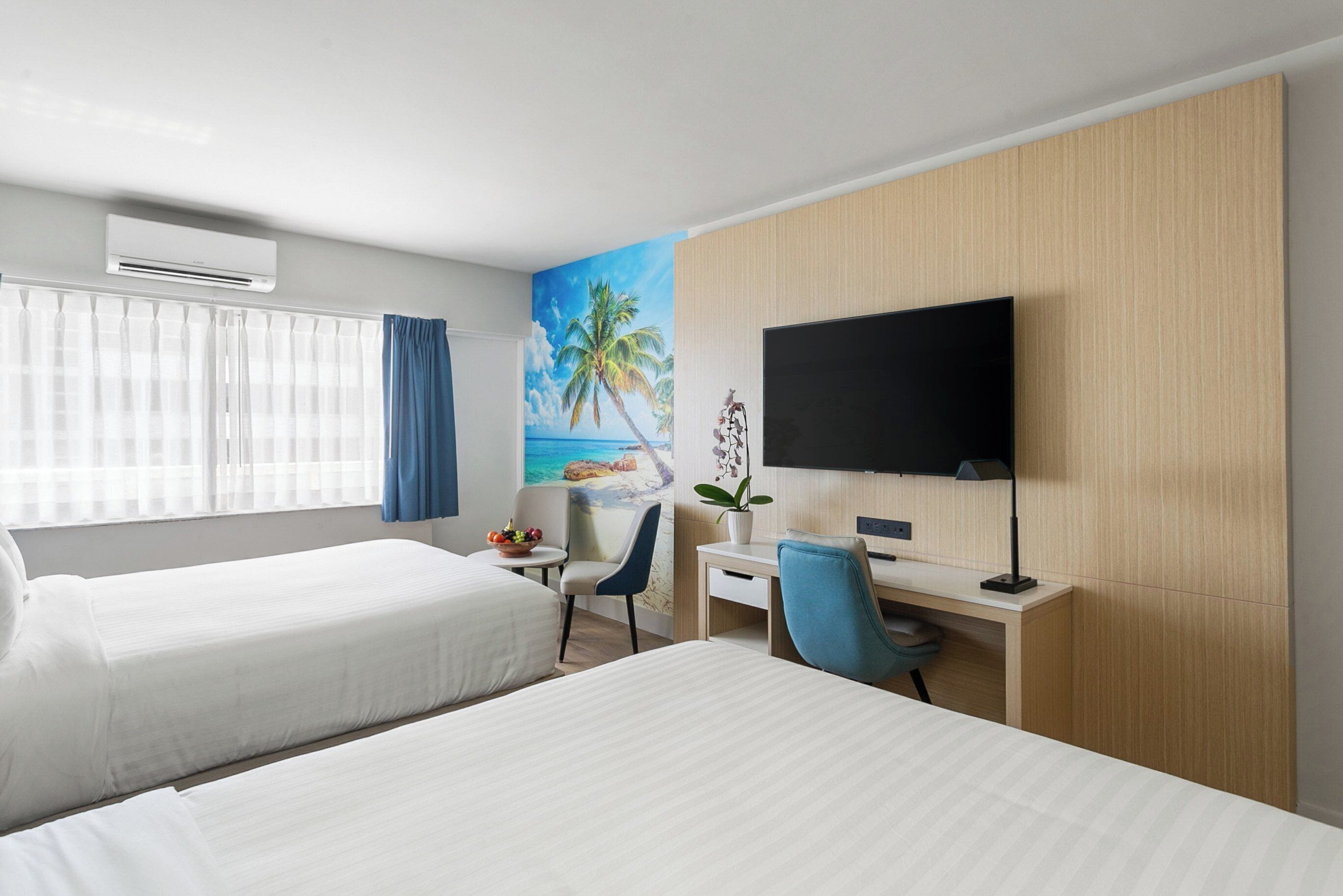 Habitación de hotel con dos camas, un escritorio, una silla, un televisor y un ventanal con cortinas.