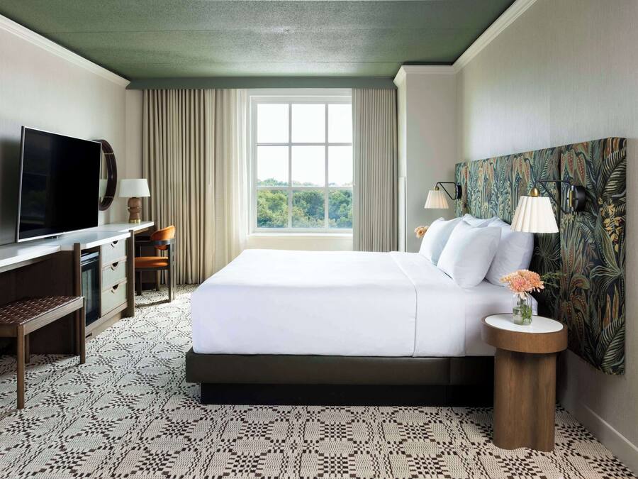 Una habitación de hotel con cama, televisión, escritorio y ventana con cortinas.