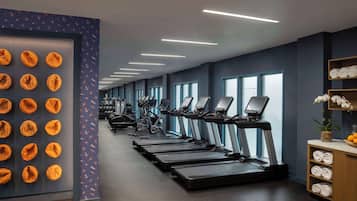 A gym with multiple treadmills, exercise bikes, and a wall with orange circular objects.