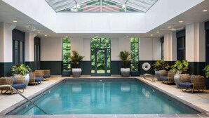 An indoor swimming pool with a glass ceiling, surrounded by wicker chairs and potted plants. - Hyatt Regency Greenwich (Old Greenwich)