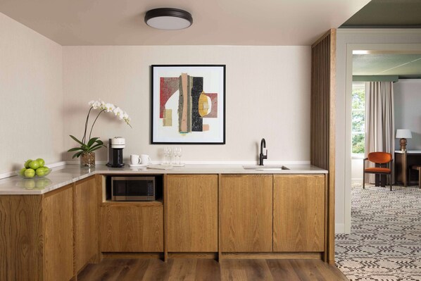 A modern kitchen with wooden cabinets, a microwave, and a coffee maker. There is a framed abstract painting on the wall and a potted orchid on the counter.