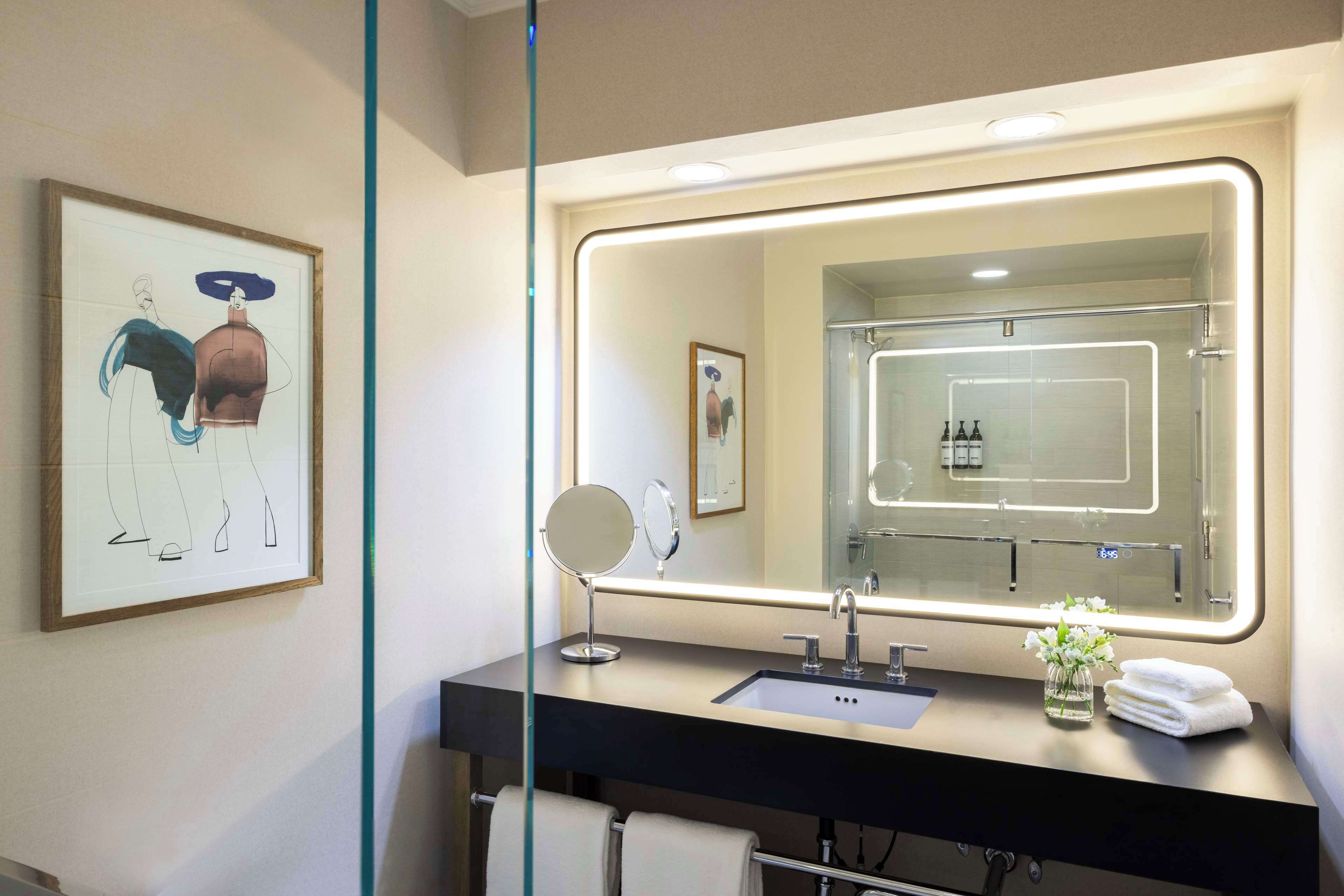 A modern bathroom with a large mirror, a sink, and a framed artwork on the wall.