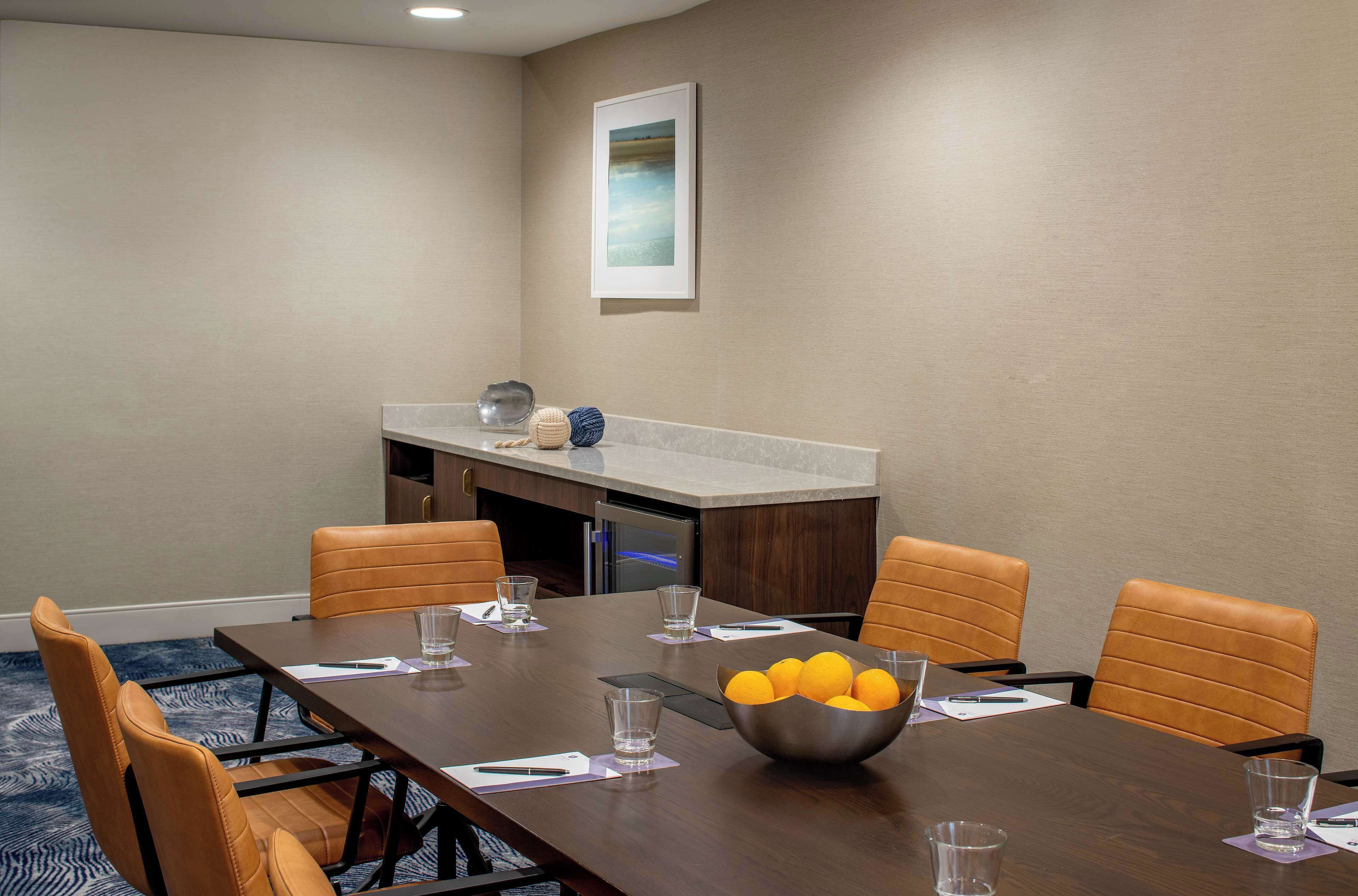 Une salle de conférence avec une longue table, six chaises, un saladier rempli d’oranges et un tableau accroché au mur.