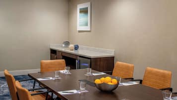 Une salle de conférence avec une longue table, six chaises, un saladier rempli d’oranges et un tableau accroché au mur.