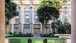 A courtyard with a central pathway, surrounded by greenery and a building with large windows and columns. - Hyatt Regency Greenwich (Old Greenwich)