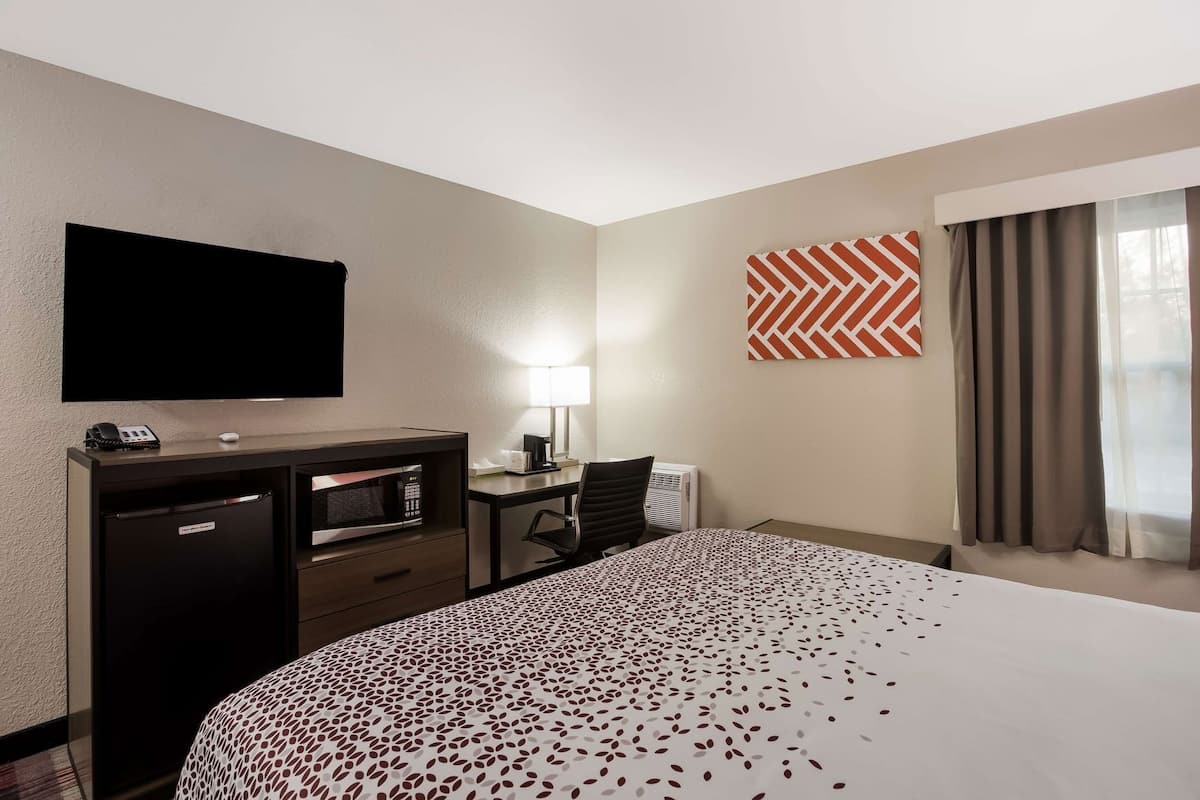 A hotel room with a bed, a desk, a TV, a minibar, and a window with curtains.
