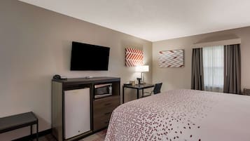 Habitación de hotel con cama, escritorio con lámpara, televisor de pantalla plana, minibar y ventana con cortinas.