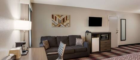 A hotel room with a sofa, a desk with a lamp, a television, a microwave, and a bed with a patterned bedspread.
