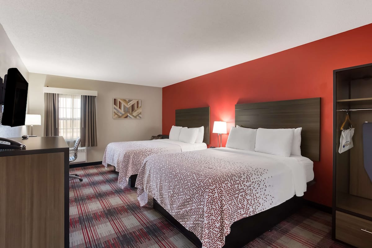 A hotel room with two beds, a desk, a chair, a TV, and a wardrobe.
