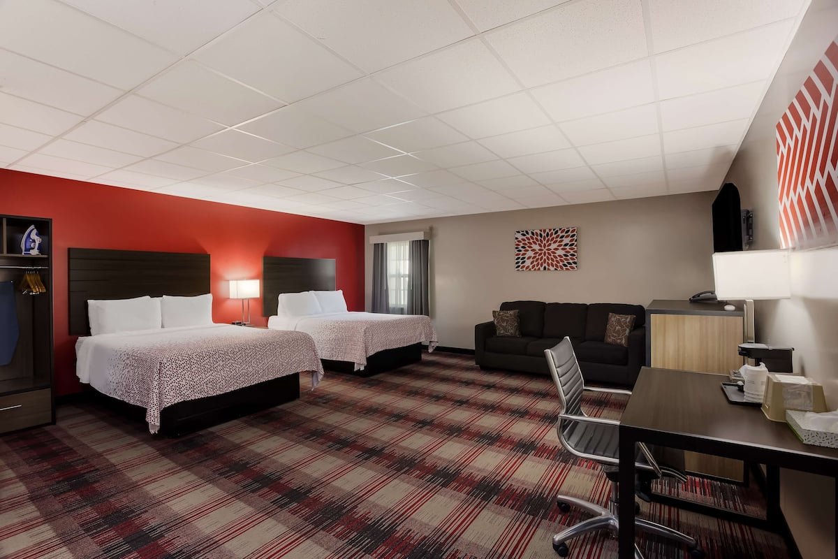 A hotel room with two beds, a desk, a sofa, a TV, and a window with curtains.