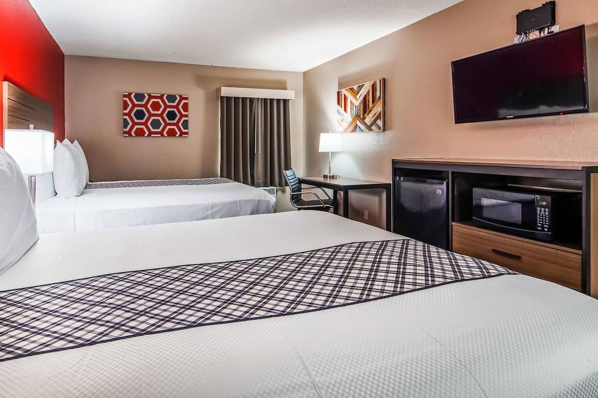 A hotel room with two beds, a desk with a chair, a TV, a microwave, and a window with curtains.