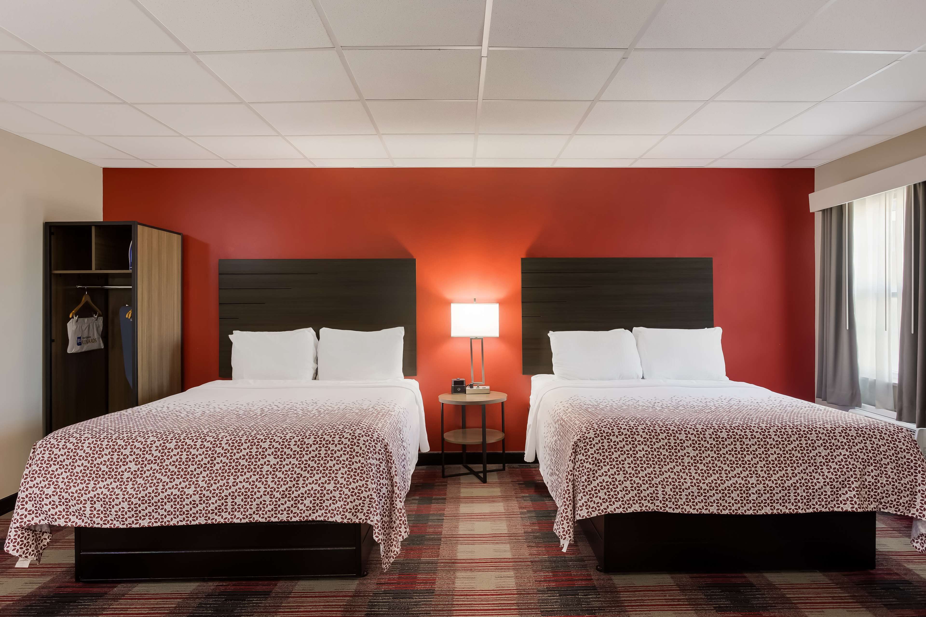A hotel room with two beds, a small table, a lamp, and a wardrobe.