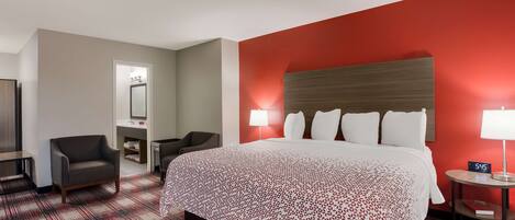 Habitación de hotel con una cama grande, un escritorio con una silla, una mesita de noche con una lámpara y una pared de acento roja.
