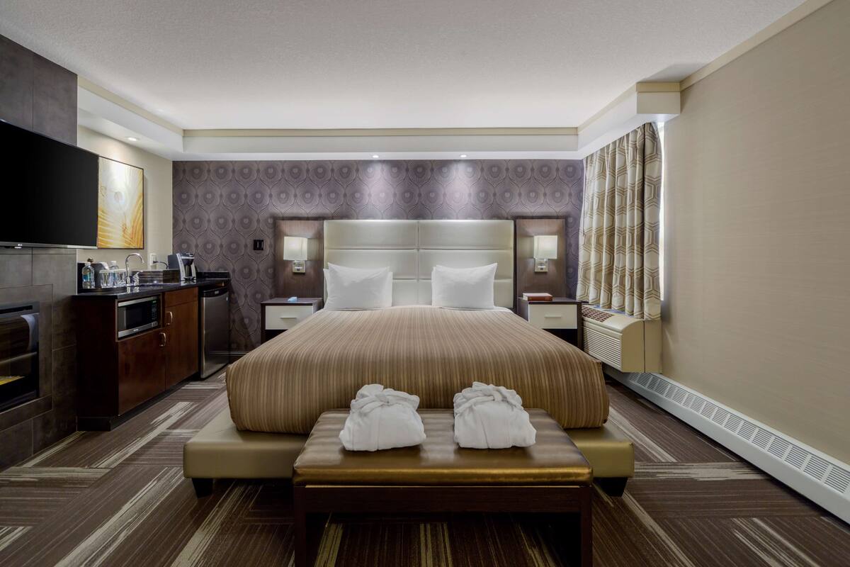 Ein Hotelzimmer mit einem großen Bett, einer Sitzbank mit Handtüchern, einem Fernseher, einer Minibar und einem Badezimmer.