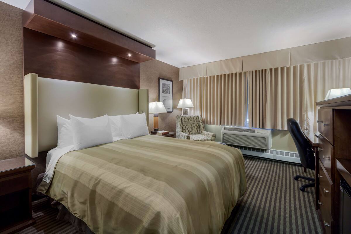 Ein Hotelzimmer mit einem großen Bett, einem Sessel, einer Klimaanlage und einem Schreibtisch.