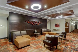 Un vestíbulo de hotel con diseño moderno, que incluye un área de estar con sofás y sillones, una alfombra estampada y una pared decorativa con jarrones.