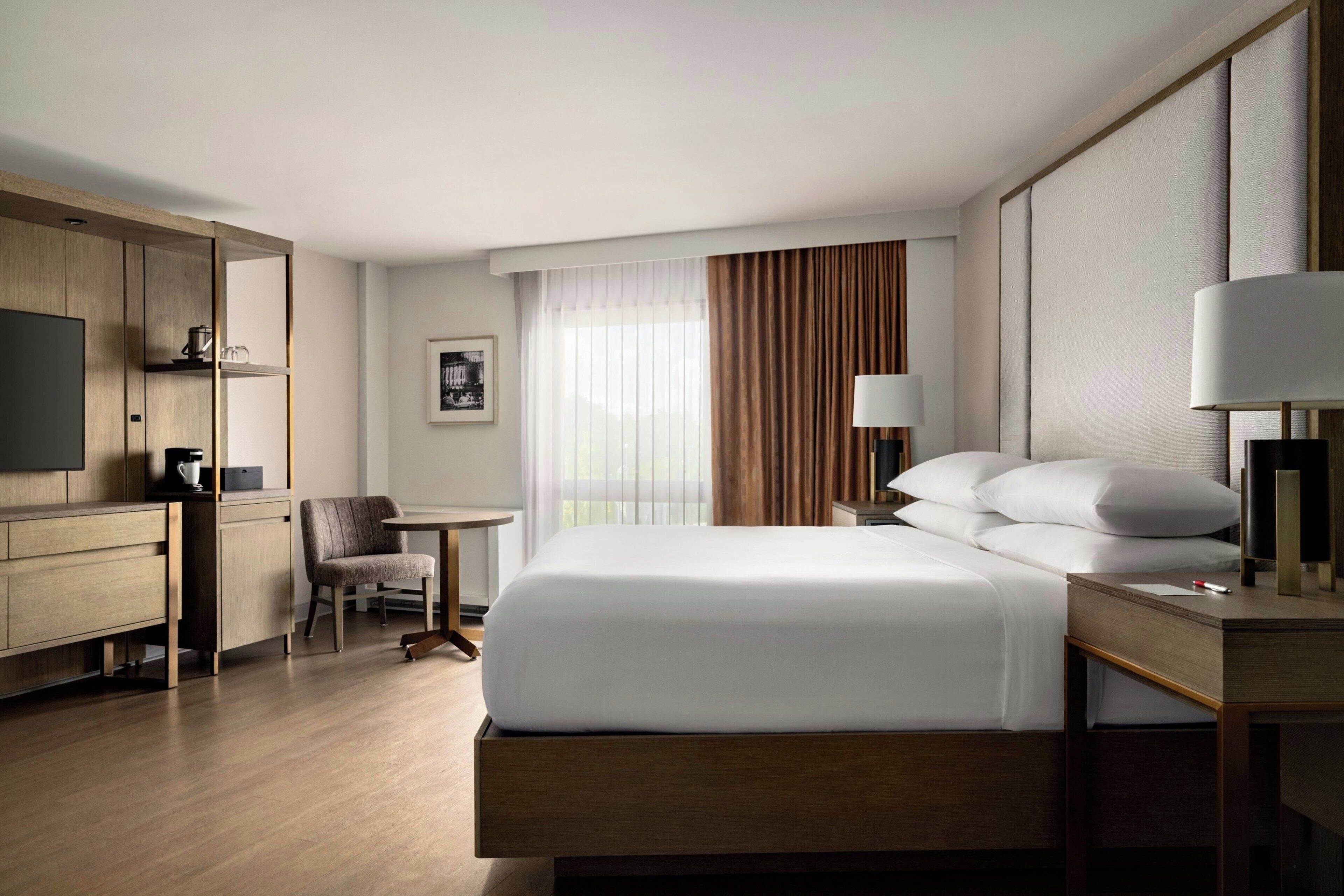A hotel room with a bed, bedside table, lamp, chair, desk, and television.
