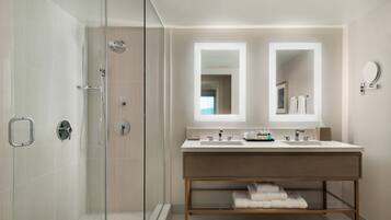 A modern bathroom with a glass-enclosed shower, a double vanity with two mirrors, and a wooden vanity with a towel rack.