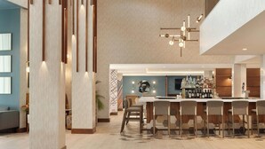A modern bar area with a long counter and multiple stools, a television, and a bar stocked with bottles. - Madison Marriott South (Madison)