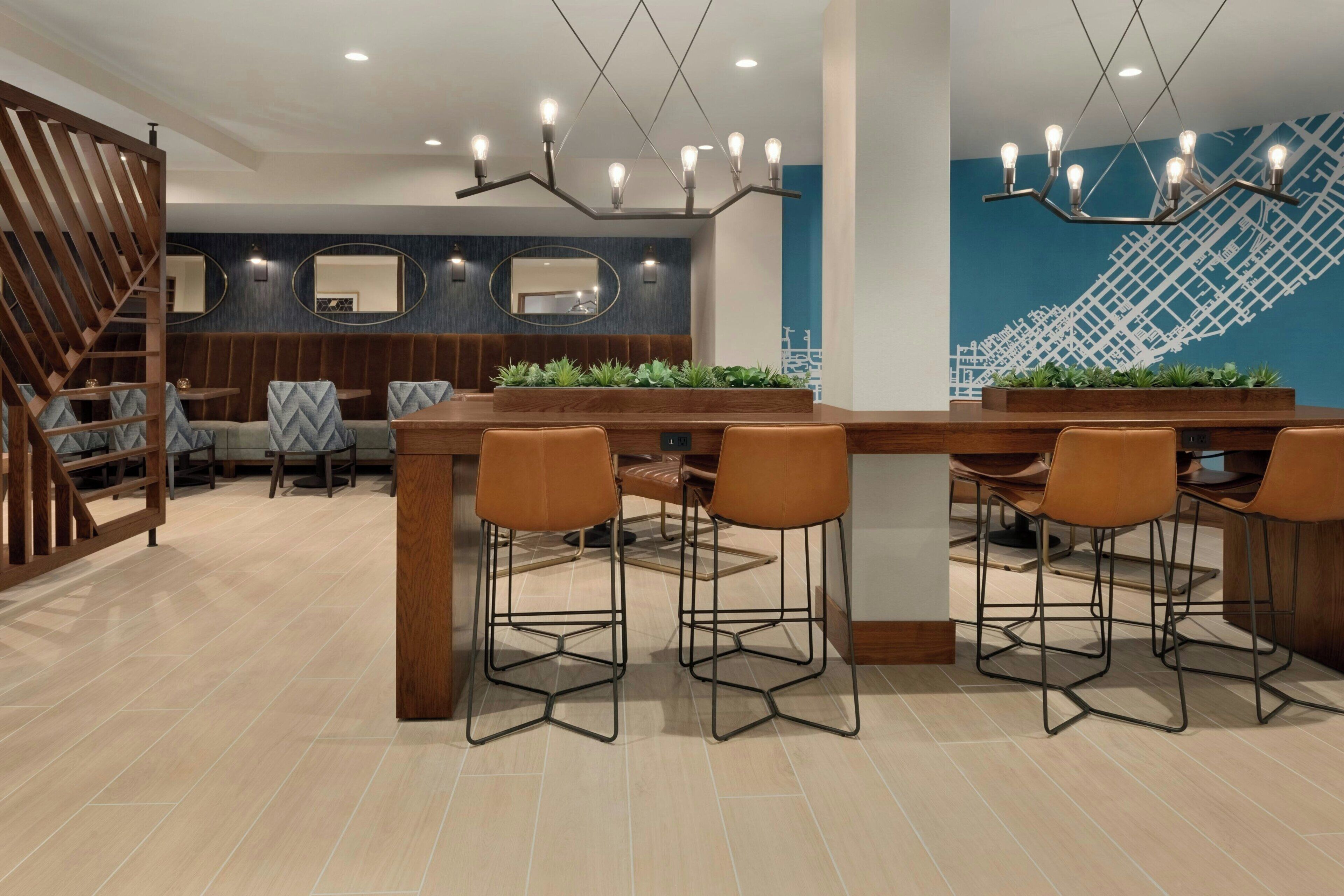 A modern dining area with a long wooden table, bar stools, and a decorative light fixture.