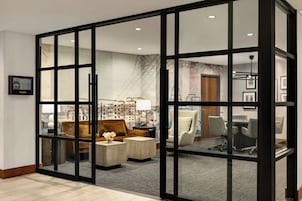 A hotel room with a glass partition, a sofa, a coffee table, and a desk with chairs.