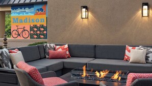 A modern outdoor seating area with a fire feature, a mural with the word "Madison," and two wall-mounted lights.