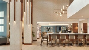 A modern bar area with a long counter and multiple stools, a high ceiling with a unique light fixture, and a visible television screen.
